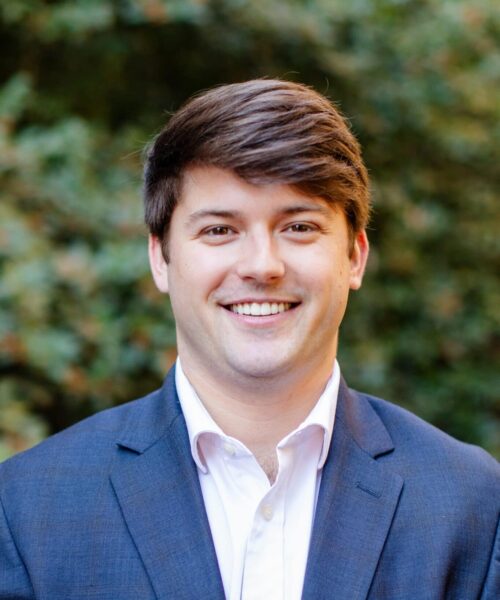 A Man Wearing A Suit And Tie Smiling At The Camera