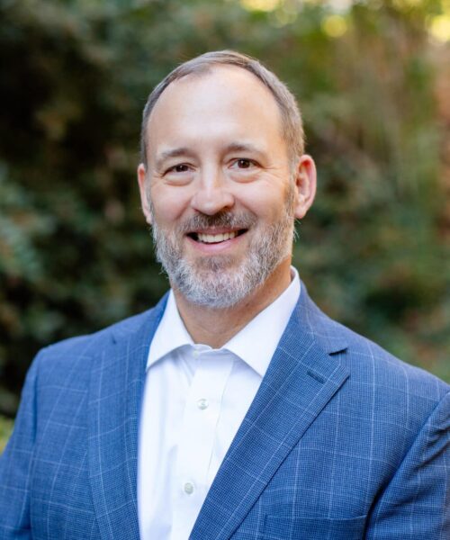 A Man Wearing A Suit And Tie Smiling At The Camera