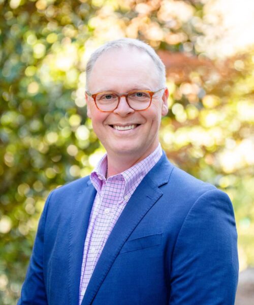 A Man Wearing Glasses And Smiling At The Camera