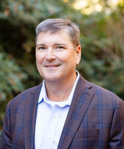 A Man Wearing A Suit And Tie Smiling At The Camera