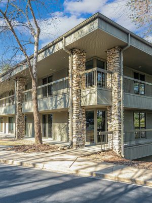 Exterior View Of A Multi-family Residential Building With Stone Accents, Surrounded By Parked Cars, Highlighting Available Residential Properties