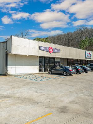 Exterior View Of A Commercial Building Featuring 'Select ABC Spirits' Signage, Surrounded By Parked Vehicles And A Wooded Area, Representing Available Commercial Real Estate Opportunities