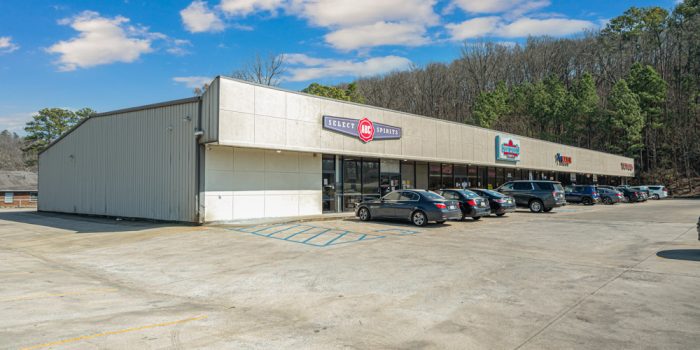 Exterior View Of A Commercial Building Featuring A Few Signage, Surrounded By Parked Vehicles And A Wooded Area, Representing Available Commercial Real Estate Opportunities
