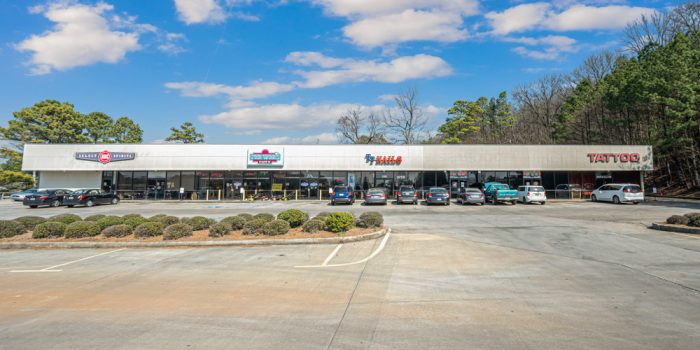 Exterior View Of A Commercial Building Featuring A Few Signage, Surrounded By Parked Vehicles And A Wooded Area, Representing Available Commercial Real Estate Opportunities