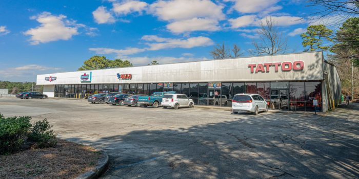 Exterior View Of A Commercial Building Featuring A Few Signage, Surrounded By Parked Vehicles And A Wooded Area, Representing Available Commercial Real Estate Opportunities