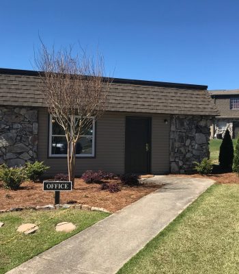 Exterior View Of A Stone-accented Office Building With A Clear Blue Sky, Featuring An 'Office' Sign In Front, Representing Red Rock Realty Group's Professional Services.