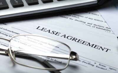 A Commercial Lease Agreement Sits Among Reading Glasses And A Keyboard On A Desk.