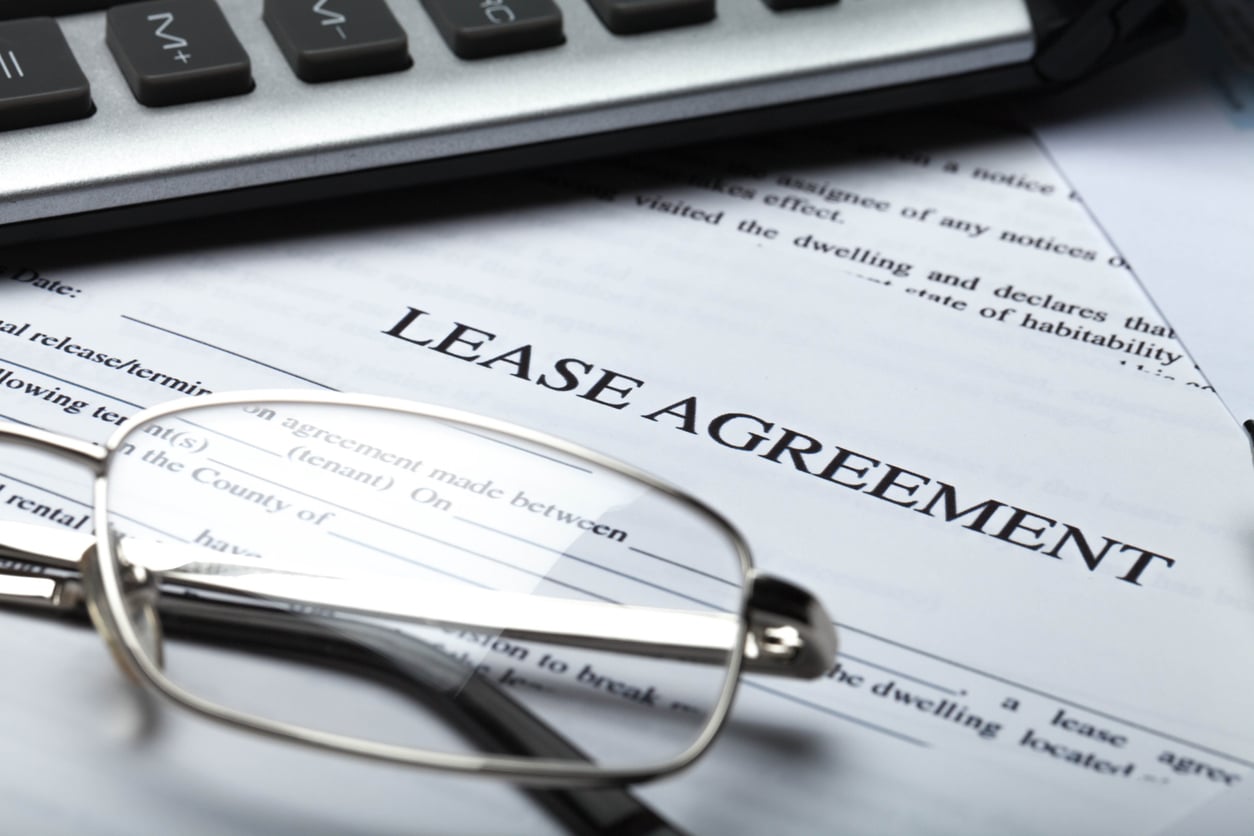 A commercial lease agreement sits among reading glasses and a keyboard on a desk.